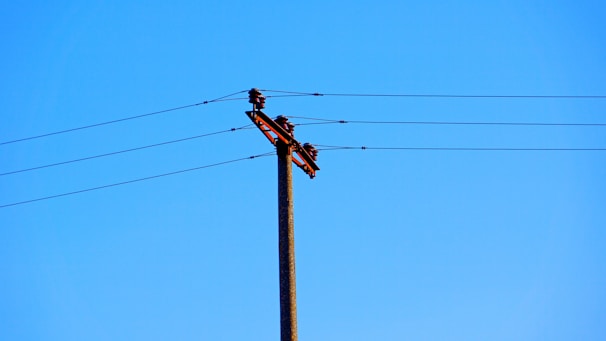 A utility pole with multiple overhead power lines set against a clear blue sky.