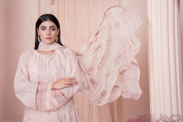Elegant South Asian woman in a soft pink flowing dress, posing confidently against a minimalist white backdrop.