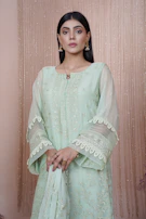 A graceful model draped in a warm cream salwar suit, standing against a soft charcoal backdrop.