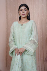 A woman gracefully modeling a deep peacock green kurti with subtle gold embroidery, standing against a warm cream backdrop.