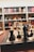A close-up of a chessboard with black and white chess pieces arranged for play. The background consists of bookshelves filled with various books, creating a cozy, intellectual atmosphere.