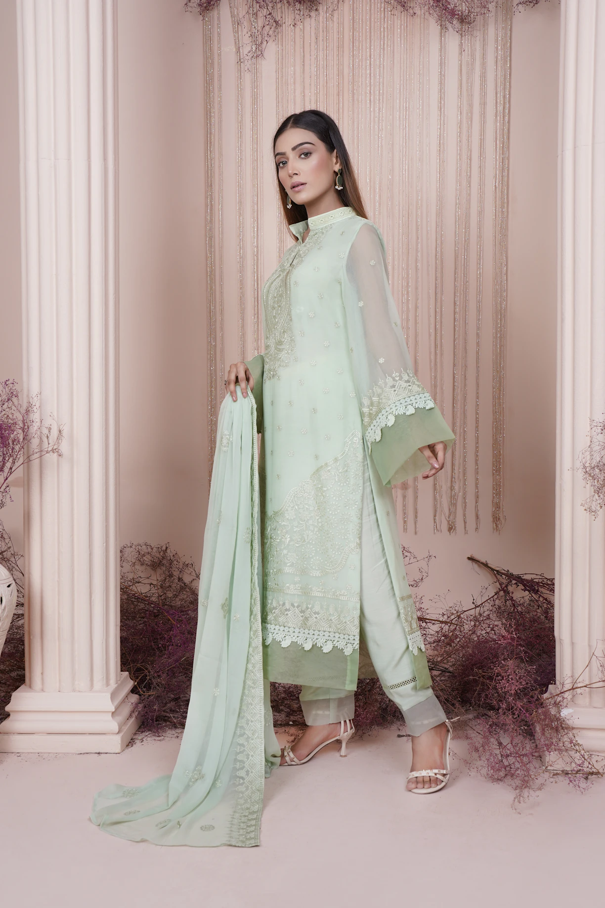 A graceful Pakistani woman wearing a cream and beige embroidered unstitched suit, standing in soft natural light.