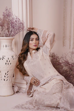 A graceful woman wearing a soft cream-colored borkha with delicate gold embroidery, standing against a minimalistic white background.