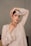 A woman is posing gracefully, wearing an elegant, embroidered beige outfit with intricate lace and mirror work. She accessorizes with large, ornate earrings and delicate jewelry. Her hand is placed artistically on her head, accentuating the design of her outfit.