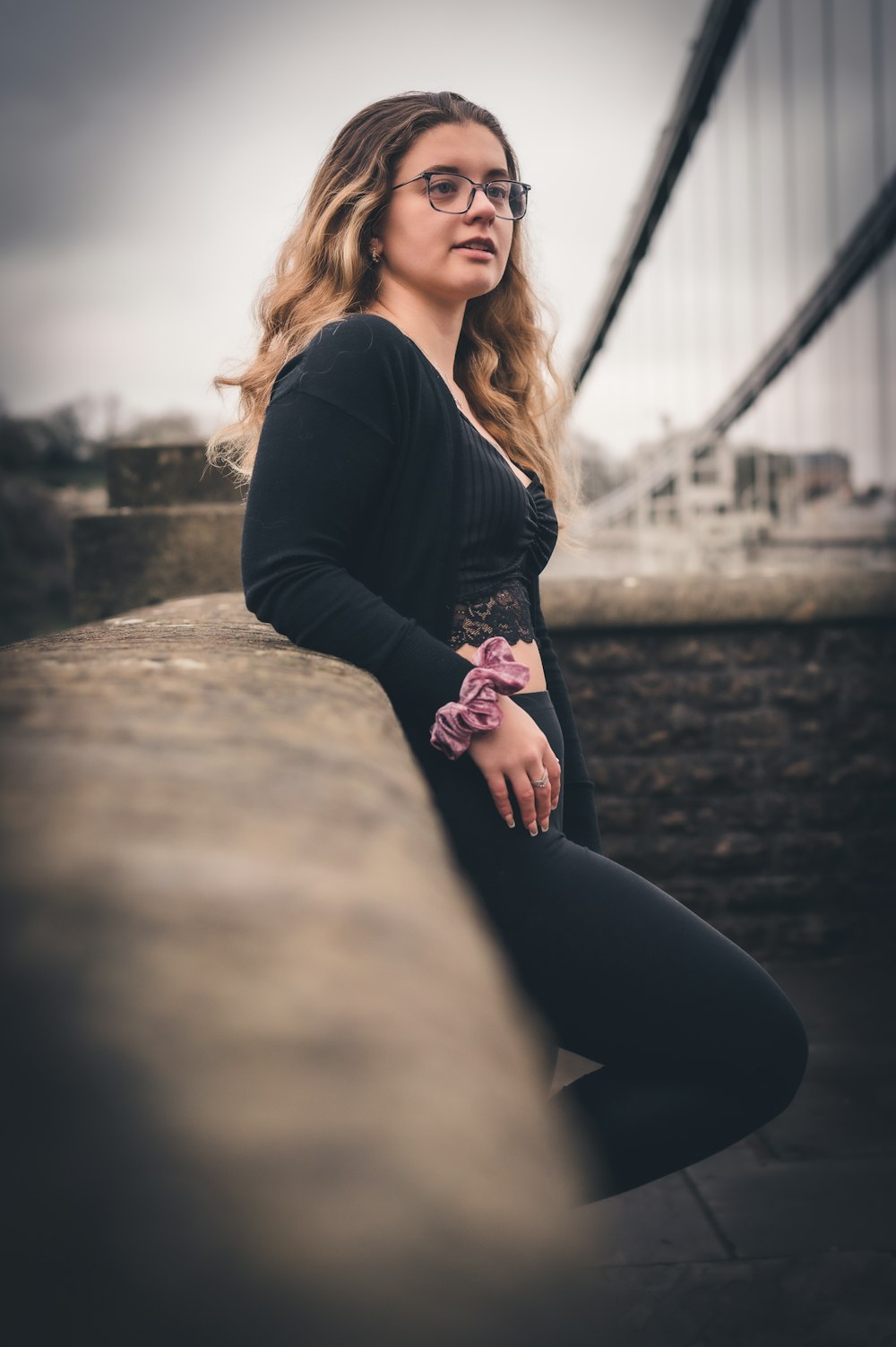 a woman sitting on a ledge with a bridge in the background