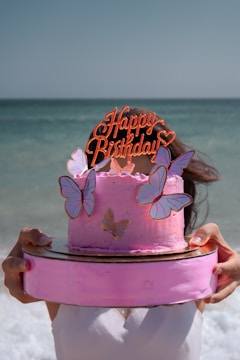 a woman holding a pink cake with butterflies on it