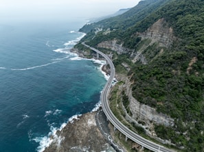 Winding coastal highway with cliffs and ocean waves crashing below, perfect for a road trip