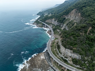 Winding coastal highway with cliffs and ocean waves crashing below, perfect for a road trip