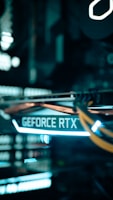 A close-up view of a computer graphics card with the text 'GEFORCE RTX' prominently displayed, featuring glowing lights and cables in a dimly lit environment.