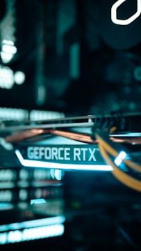 A close-up view of a computer graphics card with the text 'GEFORCE RTX' prominently displayed, featuring glowing lights and cables in a dimly lit environment.