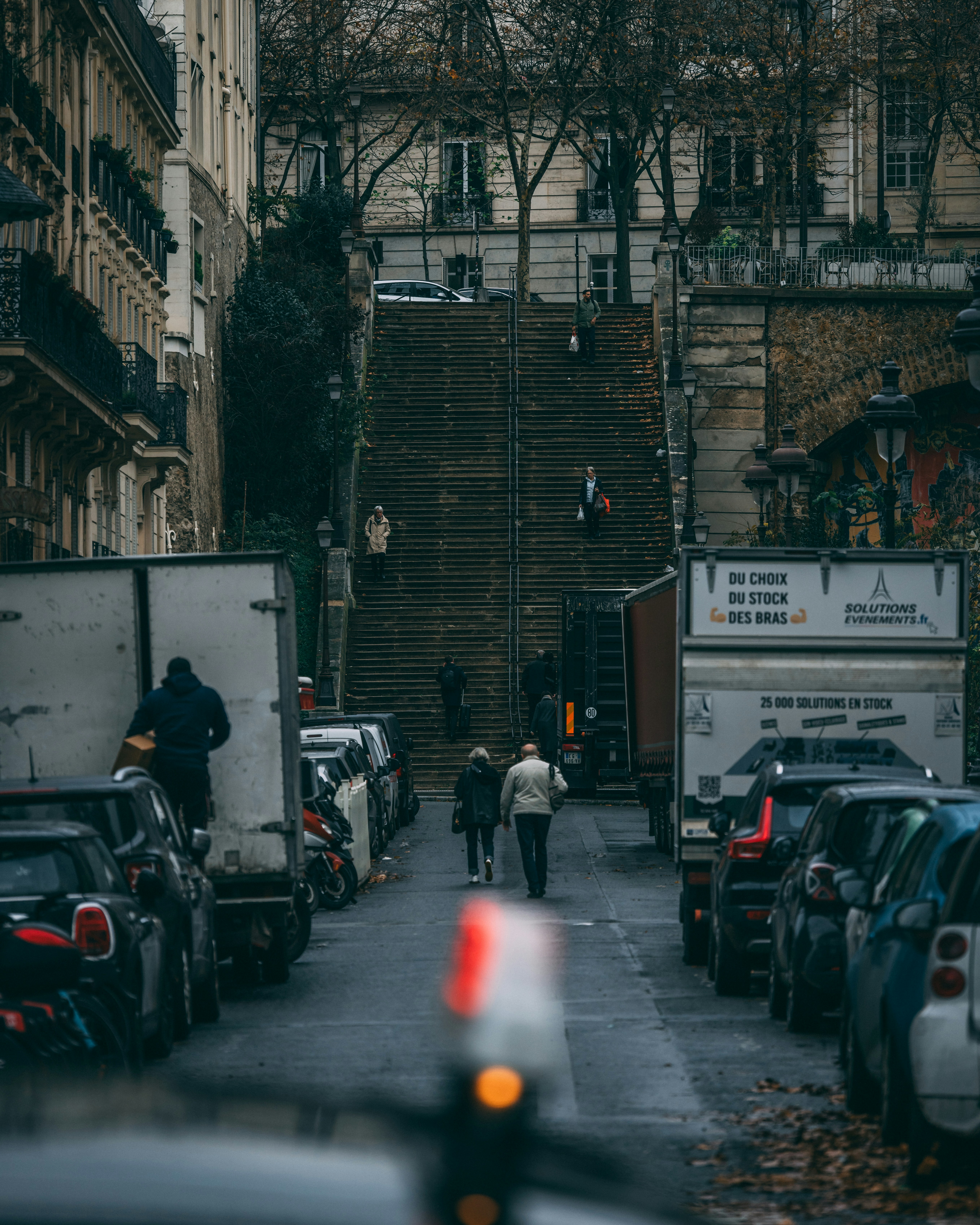 a group of people walking down a street next to parked cars