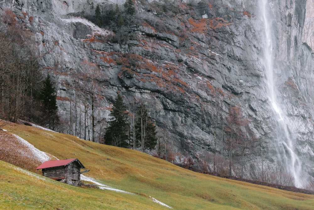 a cabin in a field with a waterfall in the background