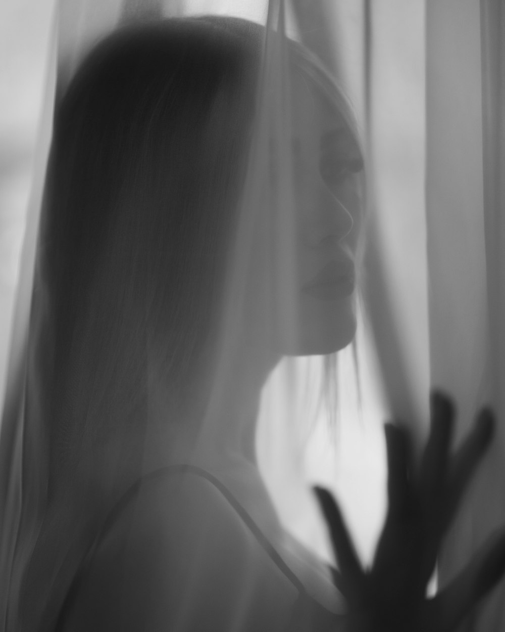 a black and white photo of a woman looking out a window