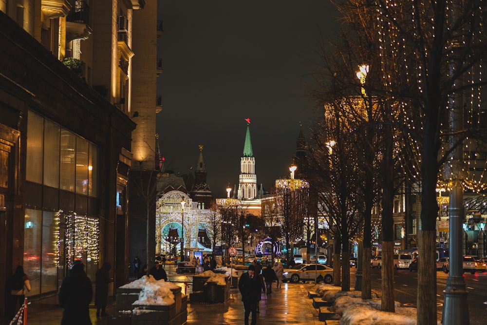 a city street at night with people walking on the sidewalk