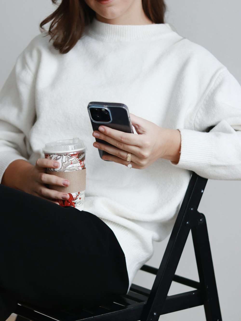 a woman sitting in a chair holding a cup of coffee and a cell phone