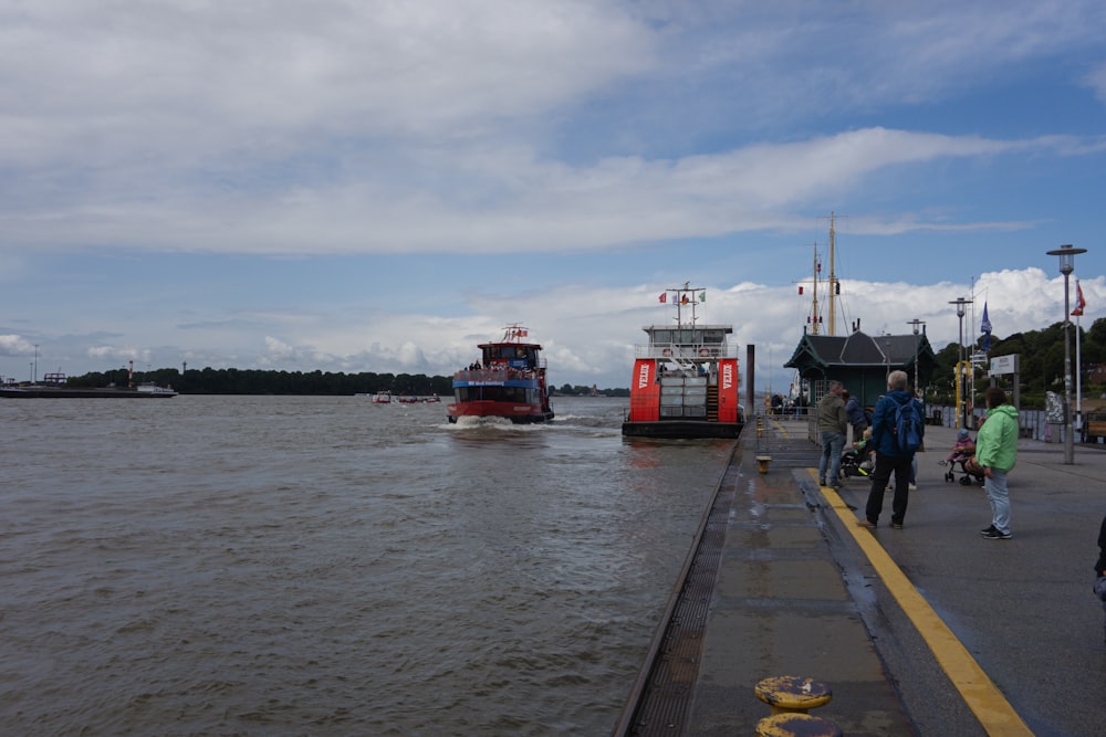 a red and white boat traveling down a river next to a pier