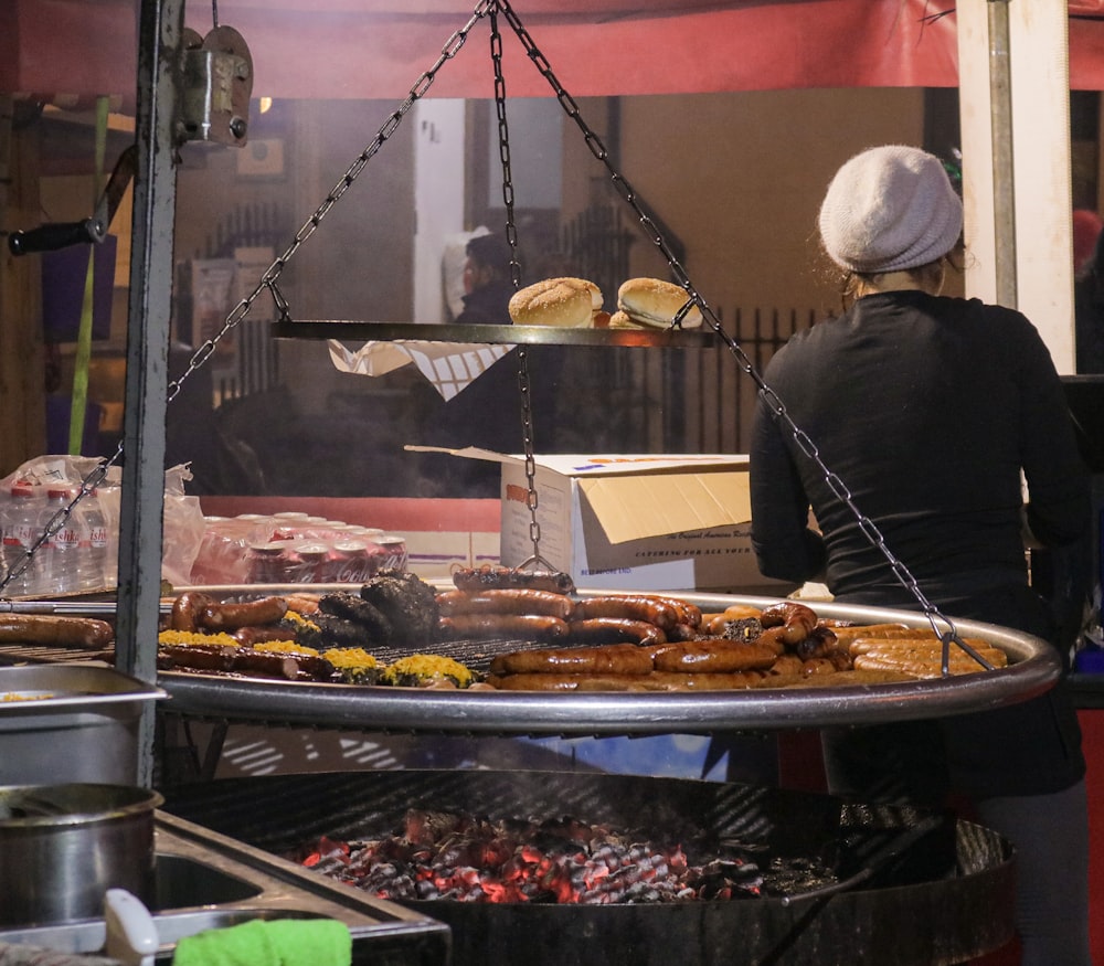 a woman standing in front of a large grill filled with food