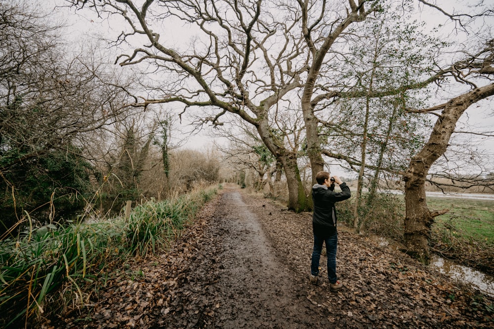 a man standing on a dirt road next to a forest