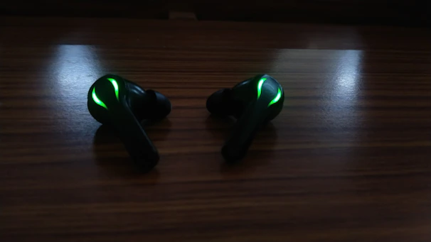 Modern wireless earbuds glowing softly with cyan light on a black surface