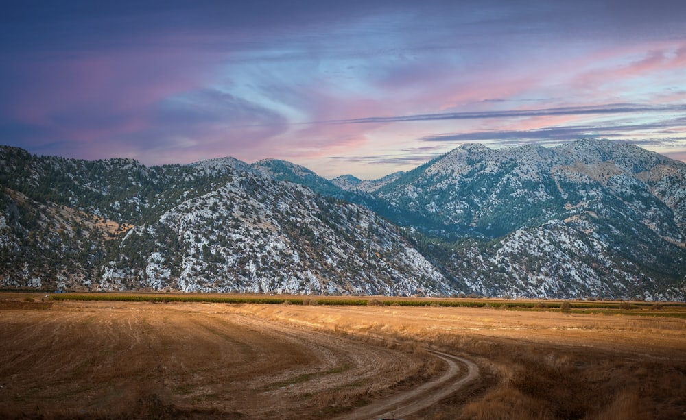 a dirt road in front of a mountain range