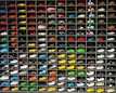 A collection of miniature toy vehicles arranged neatly in a grid of shelves. Various models of cars, vans, and scooters are displayed, featuring a wide range of vibrant colors.