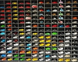 A collection of miniature toy vehicles arranged neatly in a grid of shelves. Various models of cars, vans, and scooters are displayed, featuring a wide range of vibrant colors.