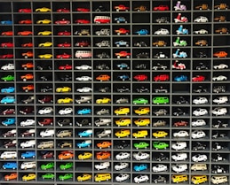 A colorful display of miniature toy cars lined up on a wooden shelf.
