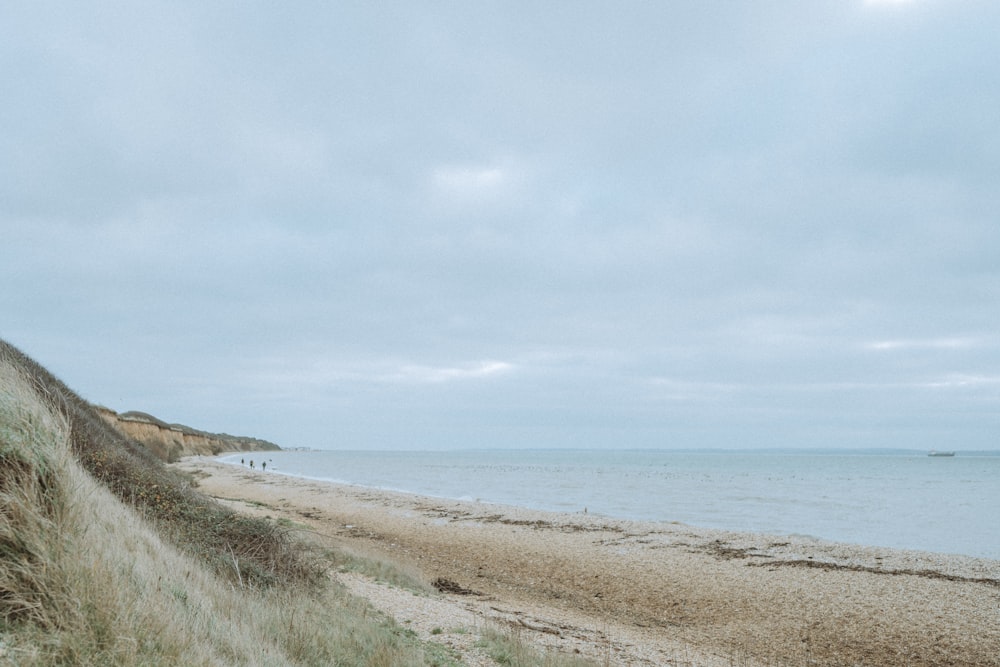 a sandy beach next to the ocean under a cloudy sky