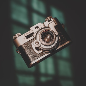 A vintage Kodak 35 camera is prominently featured, with intricate metallic details and a textured grip, set against a softly lit background with a hint of teal.