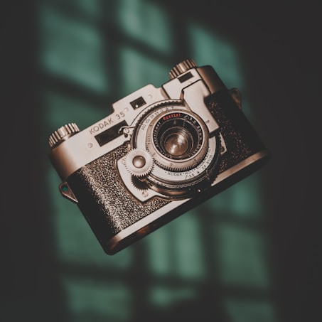 A vintage Kodak 35 camera is prominently featured, with intricate metallic details and a textured grip, set against a softly lit background with a hint of teal.