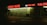 A dimly lit strip mall at night with businesses including food and liquor, payday loans, and a salon, highlighted by neon red signage reflected on wet pavement.
