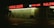 A dimly lit strip mall at night with businesses including food and liquor, payday loans, and a salon, highlighted by neon red signage reflected on wet pavement.