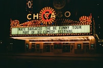 A brightly lit theater marquee displays information about Nate Bargatze's comedy tour, part of the 312 Comedy Festival. The marquee is adorned with numerous lights and features the word 'Chicago' prominently.