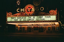 A brightly lit theater marquee displays information about Nate Bargatze's comedy tour, part of the 312 Comedy Festival. The marquee is adorned with numerous lights and features the word 'Chicago' prominently.