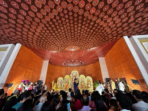 A serene gathering of devotees listening attentively to a speaker in a saffron-themed hall.