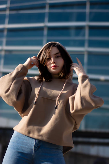 A cozy, stylish model wearing a soft beige hoodie from Gaara Comfort Clothing, standing against a minimalist urban backdrop.