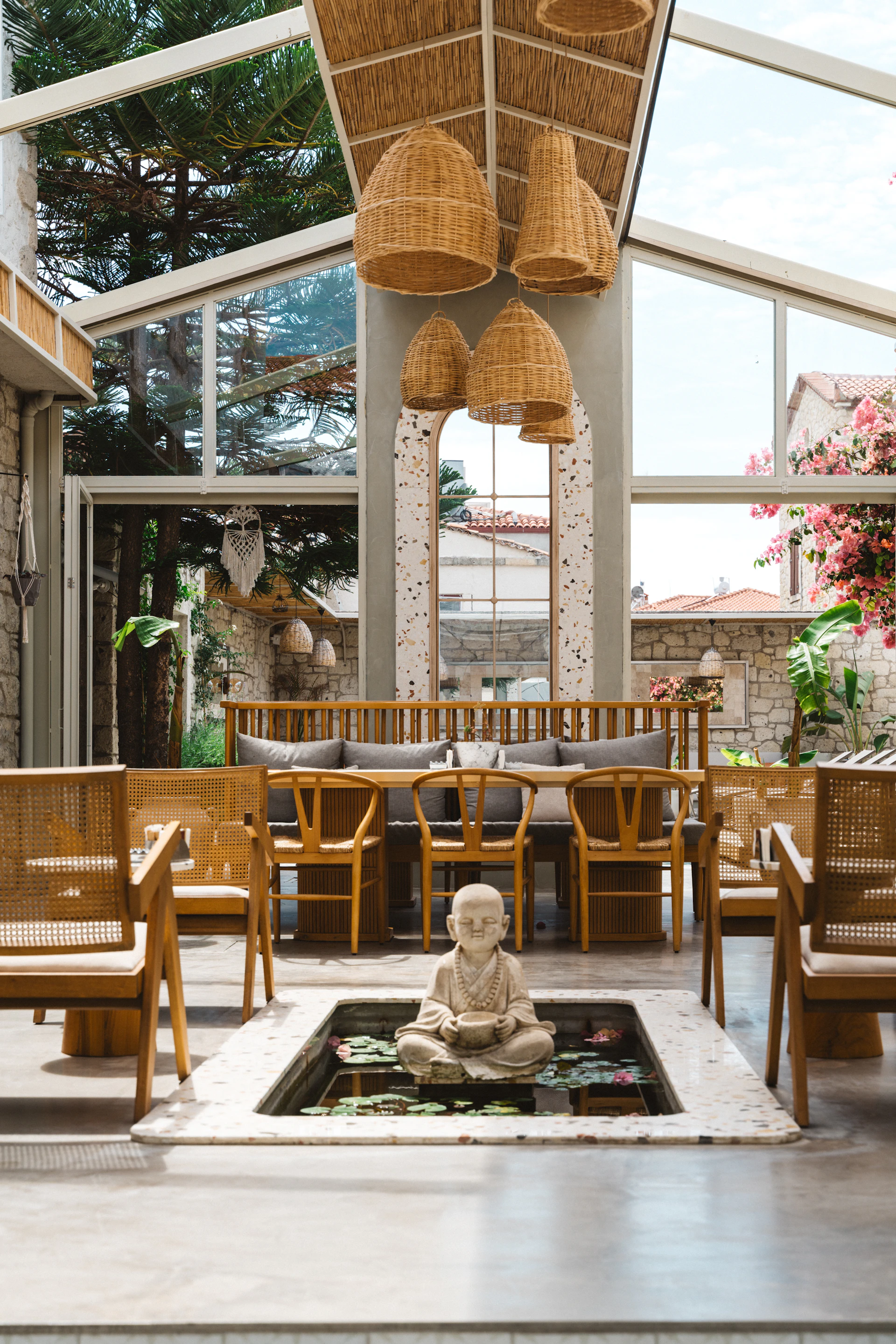 The indoor banquet area featuring elegant Balinese-style wooden seating surrounded by indoor trees and a gentle water feature creating a peaceful ambiance.