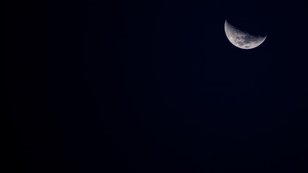 a half moon is seen in the dark sky