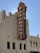 A large, vertical red and yellow sign displaying the word 'Paramount' is prominently attached to the side of an ornate, light-colored building with multiple windows. The structure features an Art Deco architectural style, with decorative elements and embellishments. The sky is clear and blue in the background.