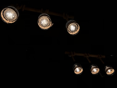 Several industrial-style hanging lights with a metal cage design are illuminated against a dark background. The lights have a warm, yellowish glow, providing a cozy ambiance.