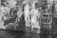A double exposure black and white photograph featuring historic brick buildings with large windows alongside a canal. Reflections and overlapping images create an artistic and layered effect, with vines and water adding texture.