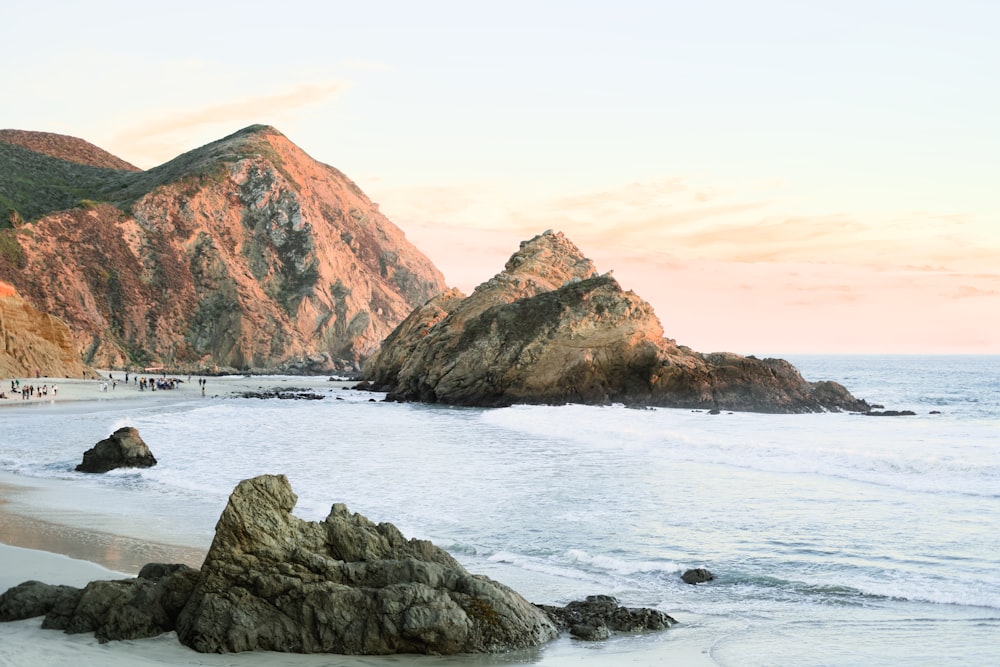 a sandy beach next to the ocean with mountains in the background