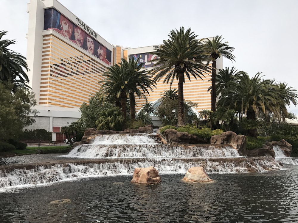 a waterfall in front of a hotel with palm trees