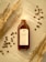 A bottle of cold brew coffee is placed on a surface surrounded by scattered coffee beans and dry wheat stalks. The label on the bottle reads 'COLD BREW BLEND COFFEE' and contains 100 ML. The scene is set in warm lighting, creating a cozy and inviting ambiance.