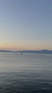 Wide-angle view of an open horizon with a boat cutting through gentle waves under warm light.