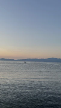 Wide-angle view of an open horizon with a boat cutting through gentle waves under warm light.