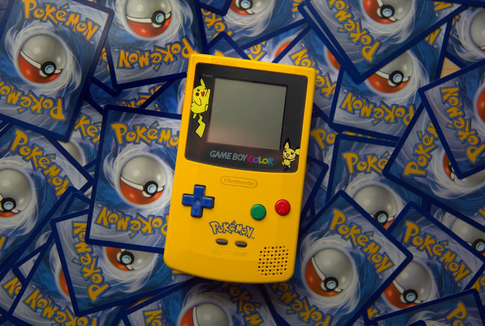 a yellow gameboy sitting on top of a pile of pokemon cards