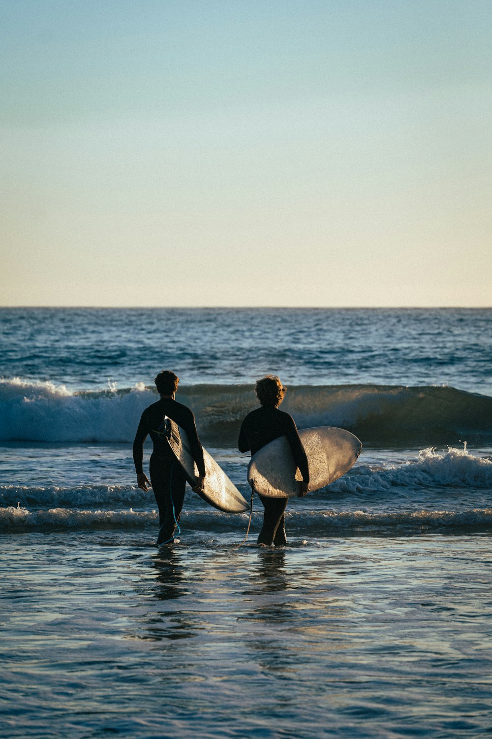 two men holding surfboards walking into the ocean