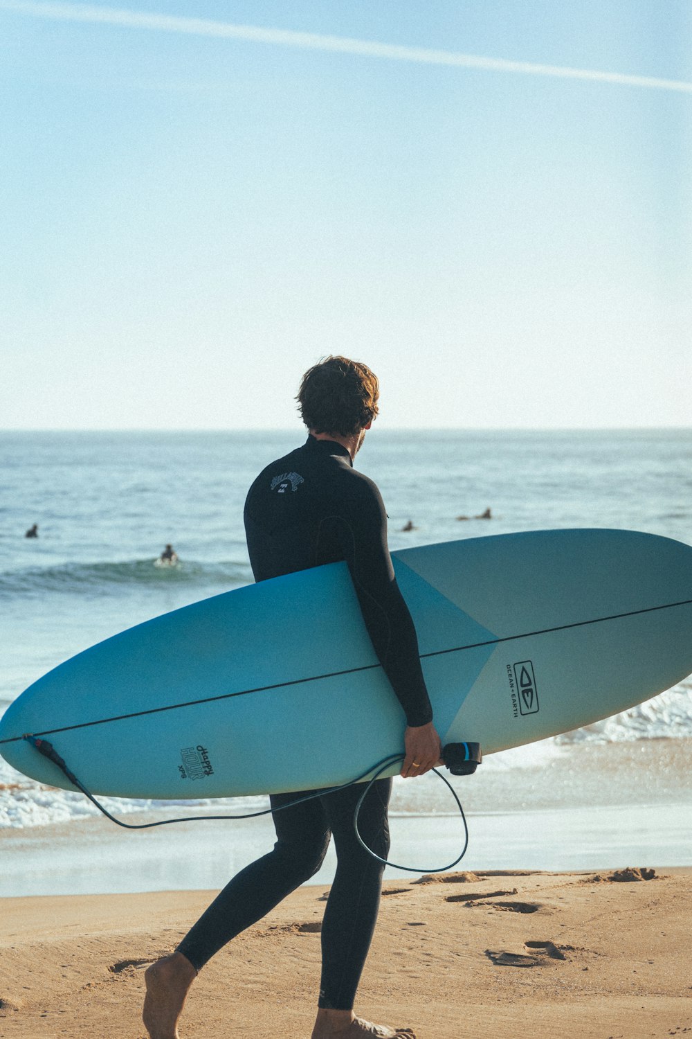 잠수복을 입은 남자가 해변에서 서핑 보드를 들고 있습니다