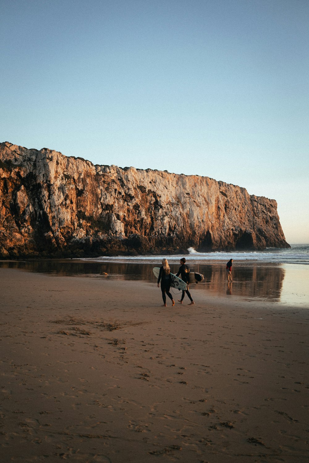 a couple of people walking across a sandy beach